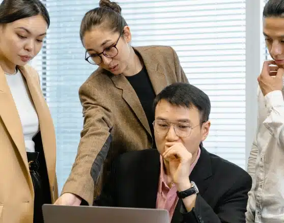 A team of four diverse business colleagues closely examining information on a laptop screen, demonstrating focused collaboration.