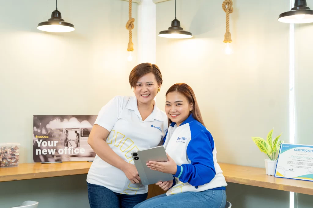 Two smiling **InsBOSS** team members collaboratively reviewing information on a tablet in their bright, modern **new office** environment.